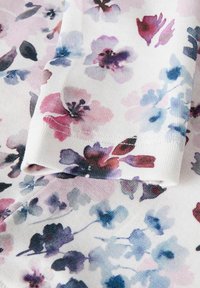 Tkanina w kwiatowy wzór z białym tłem, z delikatnymi akwarelowymi wzorami w odcieniach różu, fioletu i niebieskiego. Gładka tekstura, widoczny złożony brzeg.