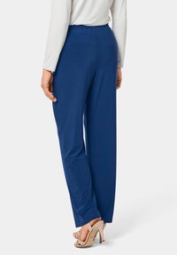 Navyblauwe, wijde broek met een elastische tailleband, gemaakt van een gladde stof. Draag met beige schoenen met hoge hakken, weergegeven vanuit de achterkant.