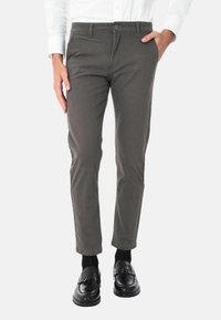 Pantaloni di cotone grigi con una vestibilità slim, dotati di chiusura con bottone e tasche laterali, abbinati a scarpe e calzini neri.