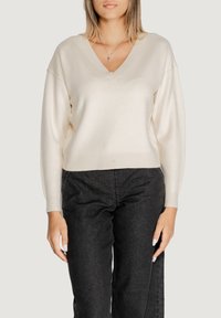 Maglione cremoso a scollo a V con maniche lunghe, tessuto morbido e polsini a costine. Abbinate a jeans scuri per un contrasto evidente.