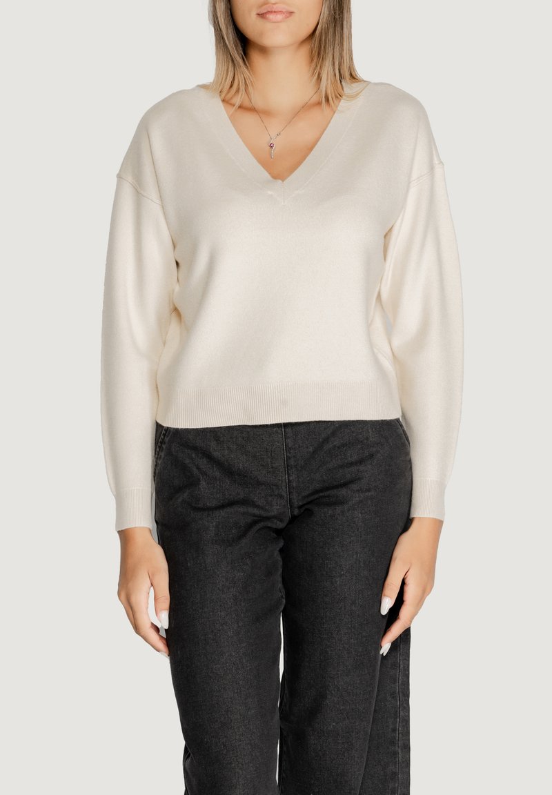 Maglione cremoso a scollo a V con maniche lunghe, tessuto morbido e polsini a costine. Abbinate a jeans scuri per un contrasto evidente.