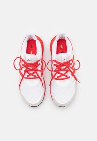 Bílé sportovní boty s červenými akcenty, s textilním svrchním materiálem, polstrovaným límcem a silnými tkaničkami, texturovanou gumovou podrážkou a logovými detaily.