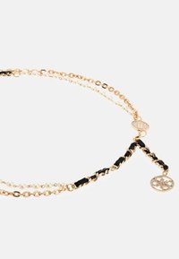 Collier doré avec des perles noires et blanches intercalées, présentant un design de chaîne texturée et un charme décoratif à l'extrémité.