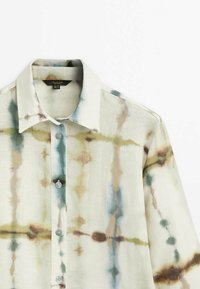 Paita valmistettu pellavasta, vaalean kermanvärisellä taustalla, jossa on vihreä, ruskea ja sininen sitruunahappokuviollinen kuvio. Sisältää terävän kauluksen ja nappikiinnityksen.