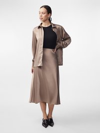 Satin beige blouse over een zwart aansluitend topje, gecombineerd met een bijpassende midi rok. Zwarte spitse schoenen maken de look af.