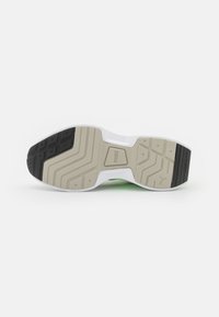 Semelle de chaussure de sport blanche avec des sections en caoutchouc texturé noir et beige ; présente un design ondulé et un logo de marque moulé dans le matériau.