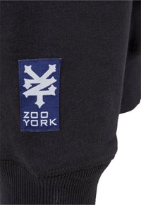 Black sweatshirt material featuring a blue rectangular patch with a white logo and text "ZOO YORK" at the lower part.