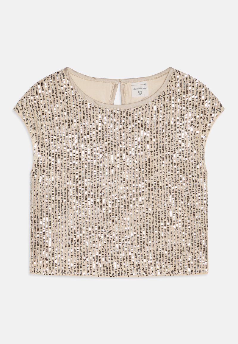 Haut beige à manches courtes orné de rangées verticales de paillettes argentées et dorées. Il présente un col rond et une petite ouverture à l'arrière.