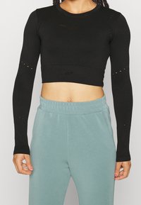 Top corto nero a maniche lunghe con ritagli in rete e logo. Abbinato a pantaloni joggers azzurri chiari, con cintura elastica e tasche laterali.