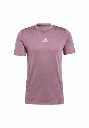 Jasnoliliowa sportowa koszulka z krótkim rękawem i okrągłym dekoltem. Posiada subtelne wzory w paski oraz białe logo Adidas na piersi. Gładki materiał.