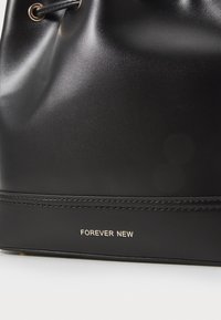 Juodas dirbtinės odos kibirėlis su auksiniais akcentais. Pasižymi lygia tekstūra, virvutės uždarymu ir iškarpytu "FOREVER NEW" logotipu.
