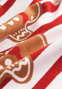 Bawełniana tkanina w czerwono-białe paski z nadrukami piernikowych ludzików w kolorze brązowym, z białym lukrem i czerwonymi akcentami, miękka w dotyku.