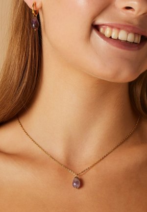 Gouden ketting met een druppelvormige paarse edelsteen hanger, gecombineerd met bijpassende creolen met een soortgelijke edelsteen.