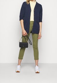Cárdigan de punto azul marino con botones, de mangas cortas, combinado con una camiseta amarilla clara y pantalones almohadillados en verde oliva. Zapatillas blancas y un bolso negro.