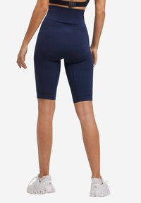 Shorts bike blu navy con un motivo testurizzato, vita alta e design aderente, abbinati a scarpe sportive bianche.