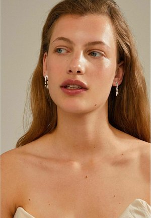 Pendientes de hilo con un acabado plateado que presentan cristales transparentes en cascada, exhibiendo un diseño delicado con una superficie texturizada.