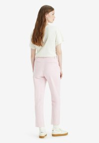 Pantaloni rosa chiaro con una vestibilità slim, tasche posteriori e una finitura liscia. Abbinati a una maglietta bianca a maniche corte e scarpe da ginnastica bianche.