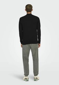 Svart långärmad topp med rund hals, i kombination med ljusgrå kordbyxor. Outfiten fulländas med krämfärgade och gröna sneakers.