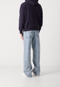 Marinblå huva sweatshirt med en känguruficka, tillsammans med ljusblå vida jeans med en utvättad look och bakfickor. Vita sneakers.