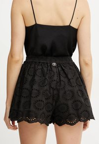 Pantaloni corti neri ricamati con orlo a scallop, caratterizzati da un motivo testurizzato di ritagli circolari e una vita elastica con hardware in argento.