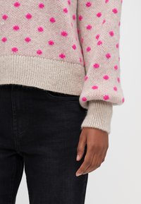Lys rosa strikket sweater med klare pink prikker, ribbede cremefarvede manchetter og kant. Båret med mørke jeans. Blød tekstur, afslappet design.