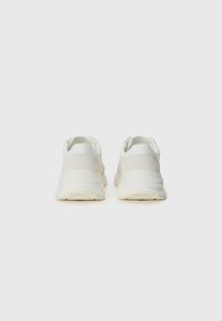 White sneakers with a textured upper, smooth accents, rounded shape, and a cushioned sole. Features a minimalist design and neutral tones.