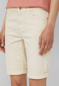 Jasne bawełniane szorty dżinsowe z podwiniętymi mankietami, posiadające zapięcie na guzik z przodu, dwie kieszenie boczne oraz kontrastowe przeszycia.