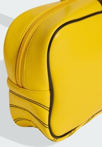 Žuta kožna torba s crnim obrubom, zaobljenim rubovima, istaknutim patentnim zatvaračem i vidljivim detaljima šavova duž bočnih stranica.