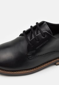 Scarpa in pelle nera con finitura liscia, punta rotonda e design con lacci neri. Include cuciture e suola di un marrone a contrasto.