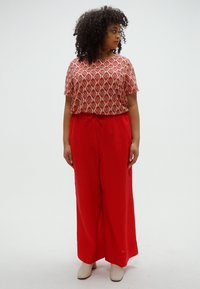 Κόκκινο παντελόνι με φαρδιά μπάτζα, συνδυασμένο με κοντομάνικη μπλούζα με γεωμετρικό σχέδιο σε κόκκινο και κρεμ χρώμα. Υφασμάτινη επιφάνεια με ρυθμιζόμενη μέση με κορδόνια.