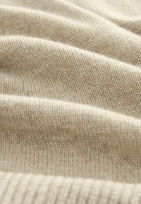 Wol brei stof in een lichte beige kleur, met een zachte textuur en zichtbare steken en milde golvingen over het oppervlak.