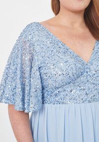 Ljusblå klänning med paljetterade detaljer på ärmarna och livstycket, V-ringning och flödande veckad kjol.