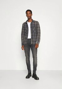 Rutete flanellskjorte i grått og svart med to brystlommer, brukt over en hvit t-skjorte, kombinert med mørkegrå skinny jeans og svarte støvler.