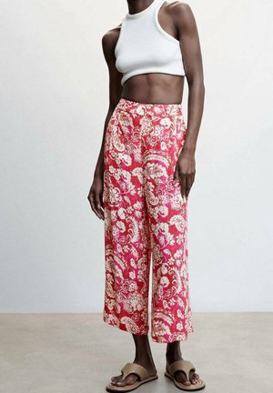 Pantalones de pierna ancha con estampado floral en rosa y blanco, tela ligera, con un ajuste cómodo, combinados con un top blanco corto y sandalias sin talón.