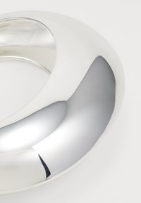 Anillo de metal plateado pulido con una superficie lisa y reflectante y un diseño redondeado, que muestra una estética contemporánea y sin costuras.