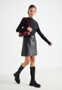 Black leather skirt, fitted long-sleeve charcoal sweater, knee-high black boots with thick soles, and a small burgundy shoulder bag.
