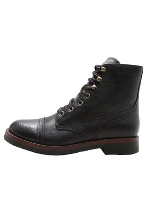 Bottine noire en cuir à lacets avec œillets métalliques, bout rond, finition texturée et semelle marron avec petit talon.
