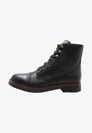 Bottine noire en cuir à lacets avec œillets métalliques, bout rond, finition texturée et semelle marron avec petit talon.