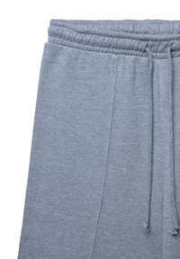 Graue Sweatpants mit elastischem Bund und Kordelzug, die die obere Hälfte und die Seitennaht auf einem weißen Hintergrund zeigen.