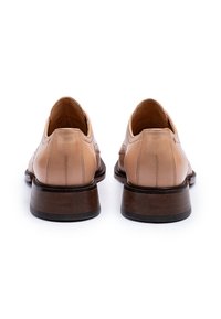 Chaussures en cuir beige au design élégant, avec une finition lisse, un bout rond et un talon en bois. Les détails de couture sont visibles.