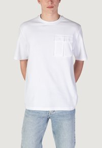 T-shirt bianco a maniche corte con scollatura rotonda e taschino sul petto anteriore con due piccole alette. Tessuto morbido con una superficie liscia.