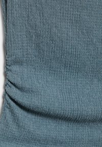 Tissu froissé bleu-vert avec une couture froncée créant de subtils plis texturés.