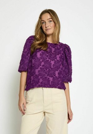 Haut texturé violet avec des manches bouffantes et un motif floral. Confectionné dans un matériau léger avec une coupe décontractée. Associé à un pantalon de couleur crème.