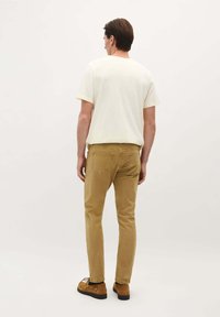 T-shirt en coton jaune clair, à manches courtes, associée à un chino beige, coupe slim, avec des poches visibles et des chaussures décontractées brunes à lacets.