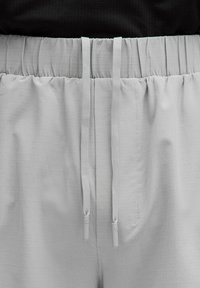 Pantalones cortos gris claro con un patrón de cuadrícula texturizada, con cinturilla elástica y cordones ajustables con puntas de plástico.