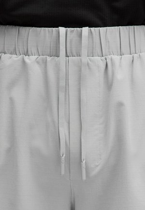 Světlé šedé šortky s texturovaným mřížkovým vzorem, mají elastický pás a nastavitelné šňůrky s plastovými konci.