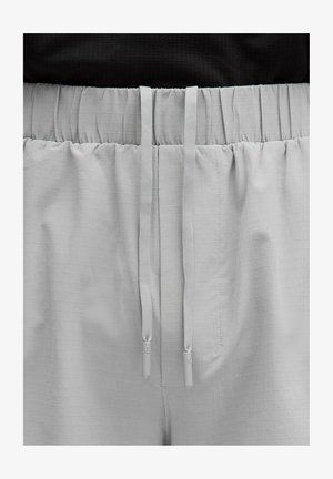 Světlé šedé šortky s texturovaným mřížkovým vzorem, mají elastický pás a nastavitelné šňůrky s plastovými konci.