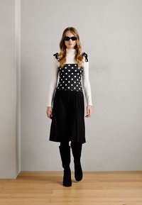 Robe à pois noir et blanc avec des bretelles volantées, portée sur un col roulé blanc, associée à des bottes noires jusqu'aux genoux. Texture lisse.