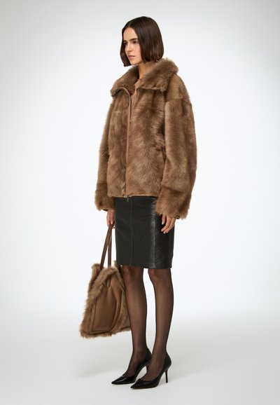 Een bruine jas van nep bont met een kraag, ritssluiting en lange mouwen. Zwarte leren kokerrok. Doorzichtige panty en zwarte pumps met puntige neus.