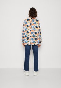 Chemise à manches longues avec un motif abstrait multicolore, présentant une coupe décontractée, un col rond et un tissu léger. Associée à un jean bleu foncé et des baskets blanches.